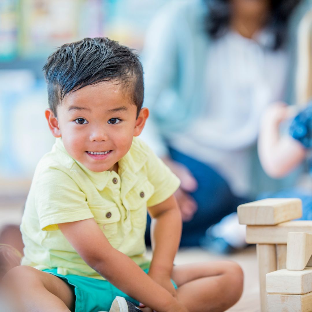 a child happily sitting on the floor playing with wood blocks